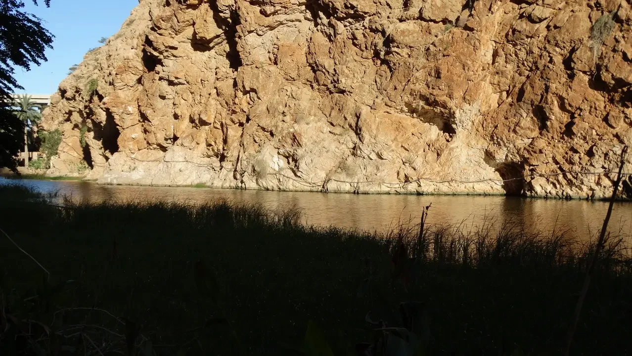 Una parete rocciosa di colore marrone chiaro si affaccia su un fiume tranquillo.