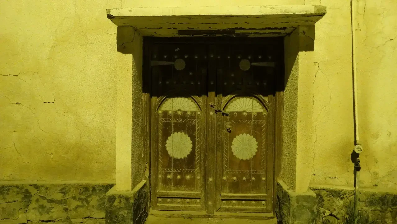 Porta in legno decorata con motivi geometrici su un muro giallo ocra.