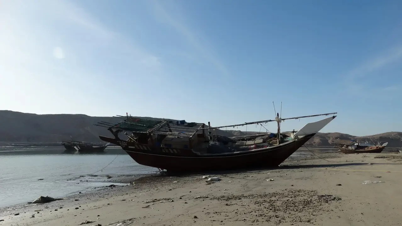 Dhows are moored on a sandy shore under a bright sky.