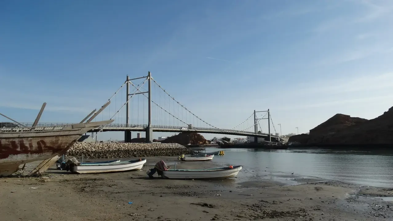 Dhows are visible in the water near a bridge structure in Oman or the Emirates.