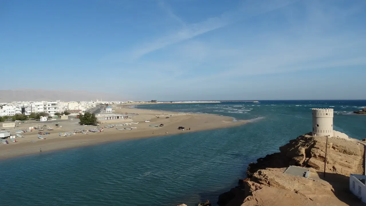 Una fortezza bianca si staglia sulla costa sabbiosa del Golfo con il mare sullo sfondo.