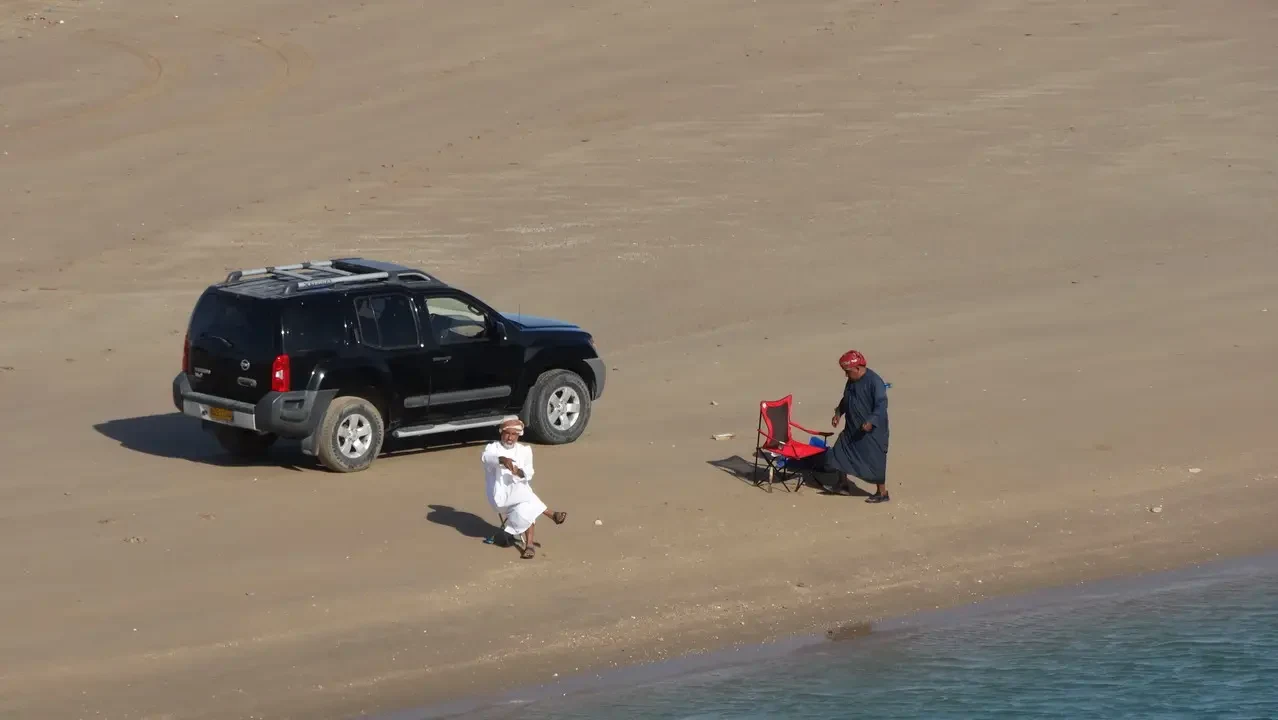 Un veicolo nero è parcheggiato sulla spiaggia con persone in abiti tradizionali.
