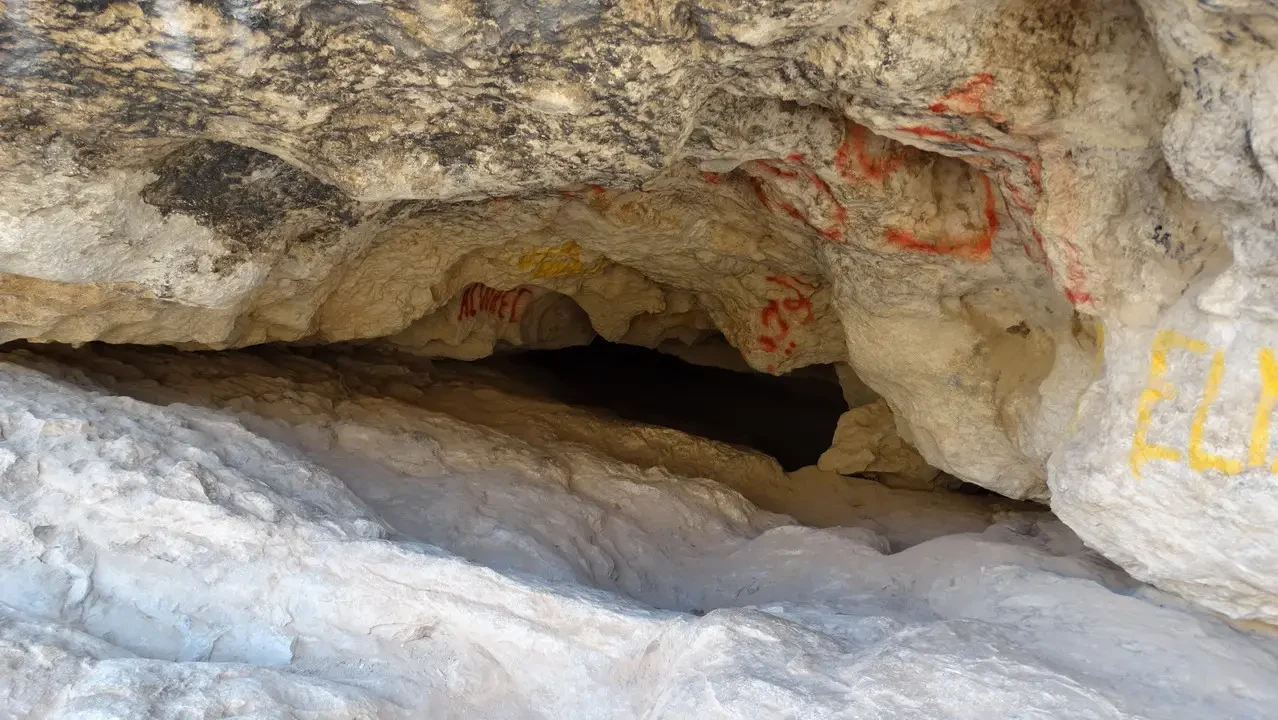 Grotta rocciosa con pareti chiare e segni rossi nella pietra.