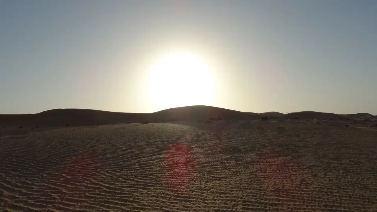 Vaste dune di sabbia si estendono sotto una luce solare intensa nel deserto.