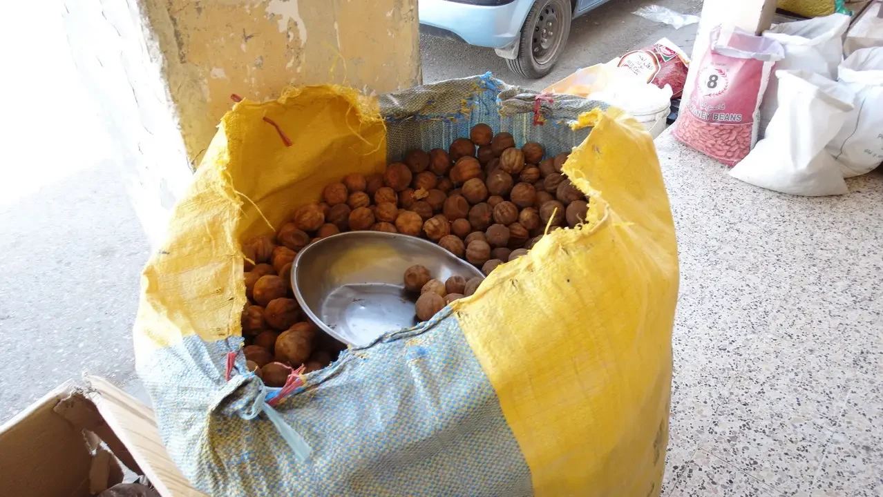 Un mucchio di noci in un sacco di tela con una ciotola all'interno.