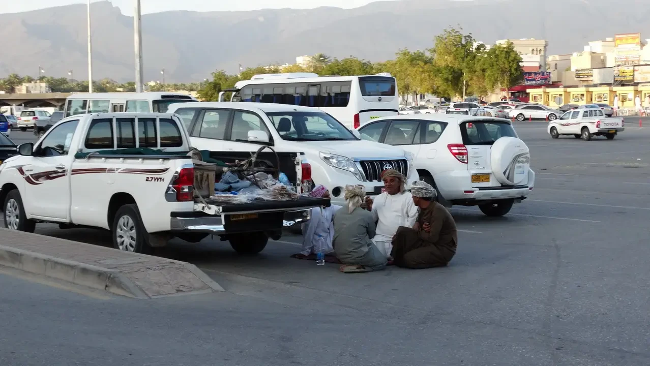 Famiglia seduta davanti a diverse auto in una strada urbana.