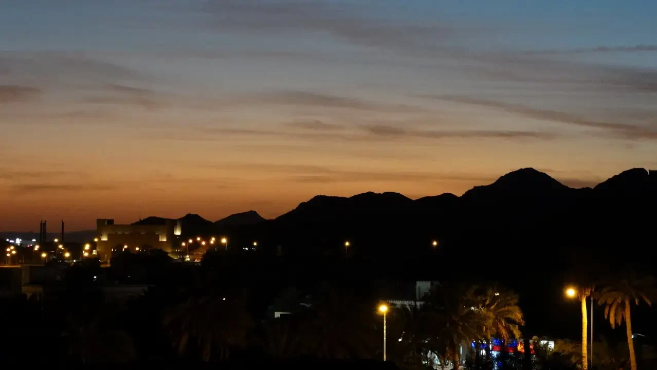 Silhouette di montagne e luci della città al crepuscolo su un paesaggio con palme.