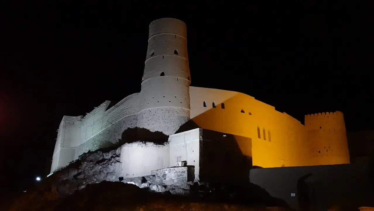 Vista notturna di una imponente fortezza con torri cilindriche e mura antiche.