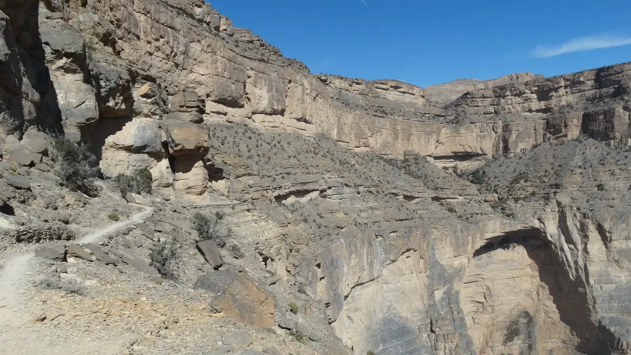 Paesaggio desertico roccioso con formazioni stratificate sotto il sole brillante.