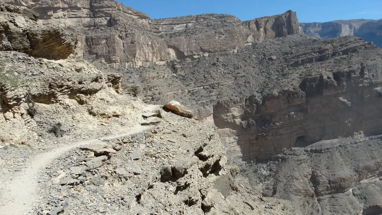 Paesaggio roccioso e arido con una strada sterrata che attraversa un canyon profondo.