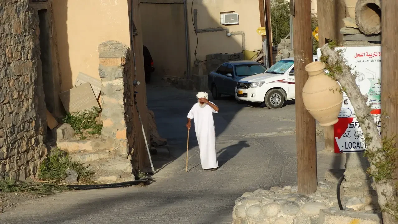 Un uomo in abito bianco cammina lungo una strada stretta con edifici in pietra.