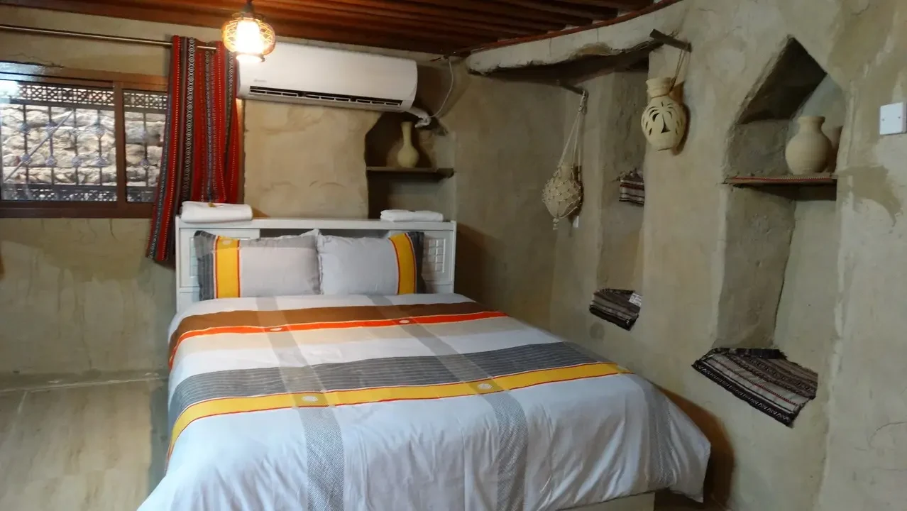 Interno rustico di una stanza con letto decorato e dettagli architettonici in stile omanita o emiratino.