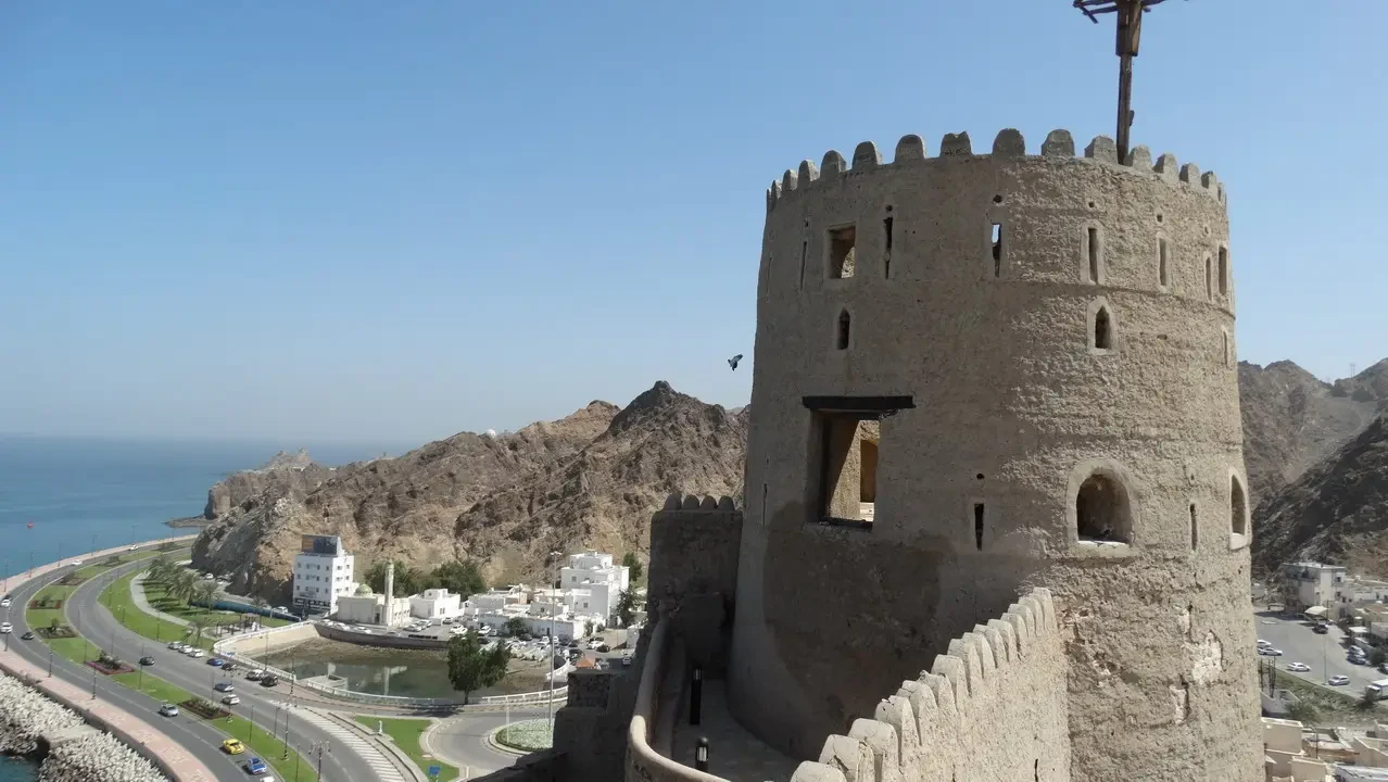 A stone fort tower dominates the arid coastal landscape of Oman.