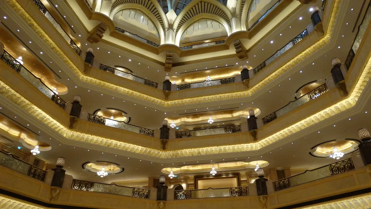 Interno sontuoso con balconate a più livelli e decorazioni dorate di un palazzo lussuoso.