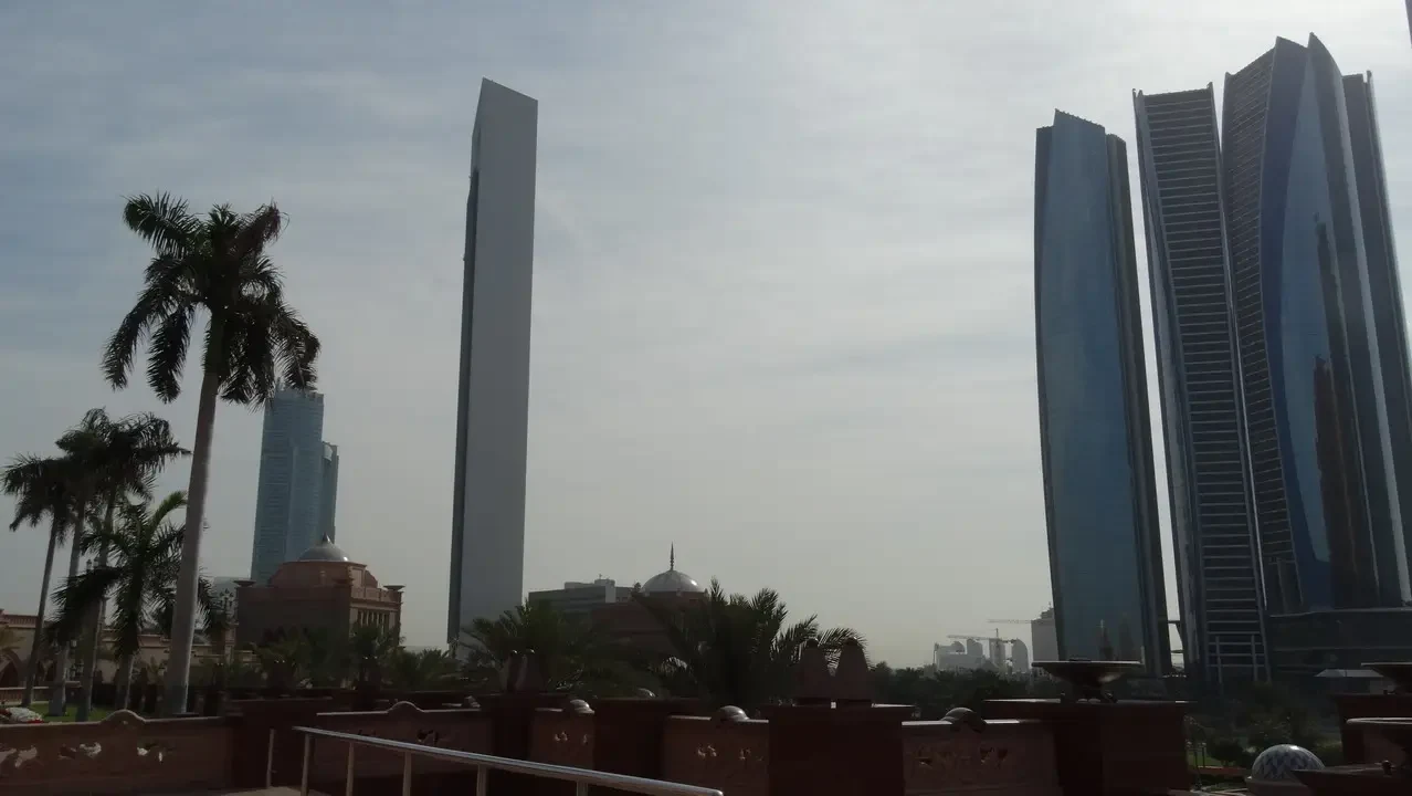 Skyline moderno di grattacieli con palme in primo piano sotto un cielo luminoso.