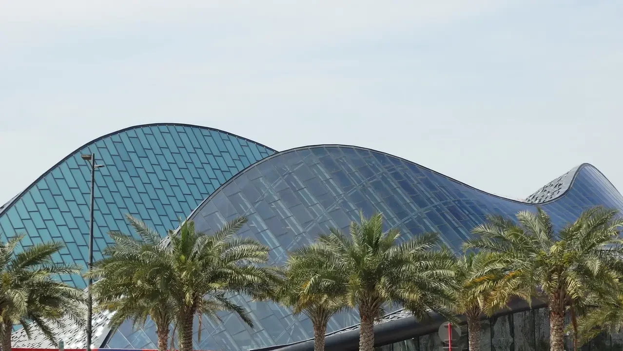 Un edificio moderno con una copertura a forma di cupola e palme in primo piano.