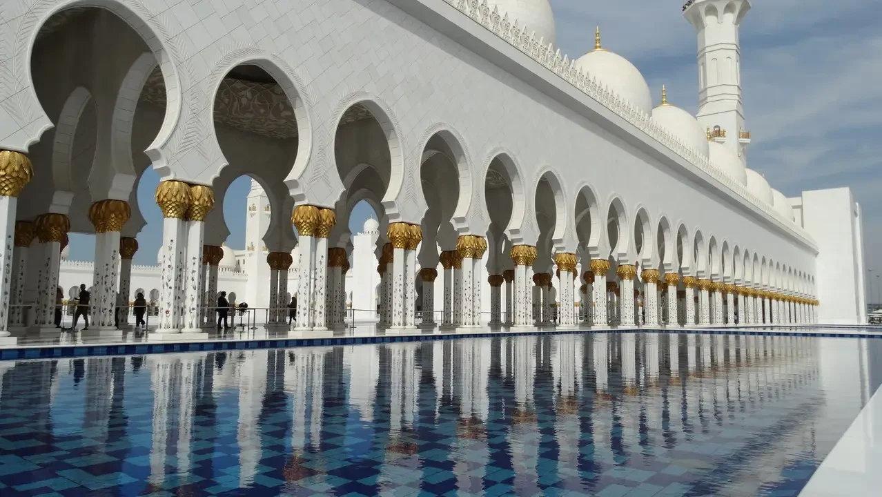 Vista esterna del Grande Moschea di Abu Dhabi con archi bianchi e dorati riflessi nell'acqua. Vista esterna del Grande Moschea di Abu Dhabi con archi bianchi e dorati riflessi nell'acqua.