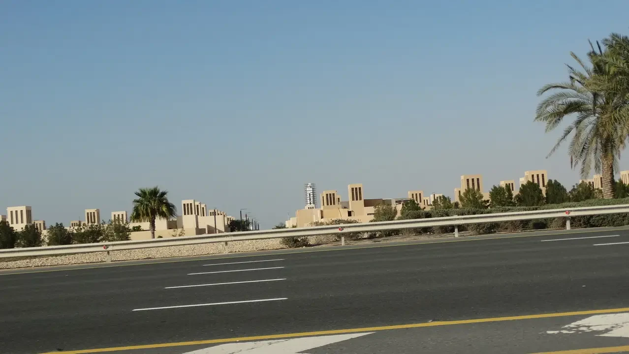 Una strada asfaltata attraversa un paesaggio urbano arido con edifici bassi e palme.