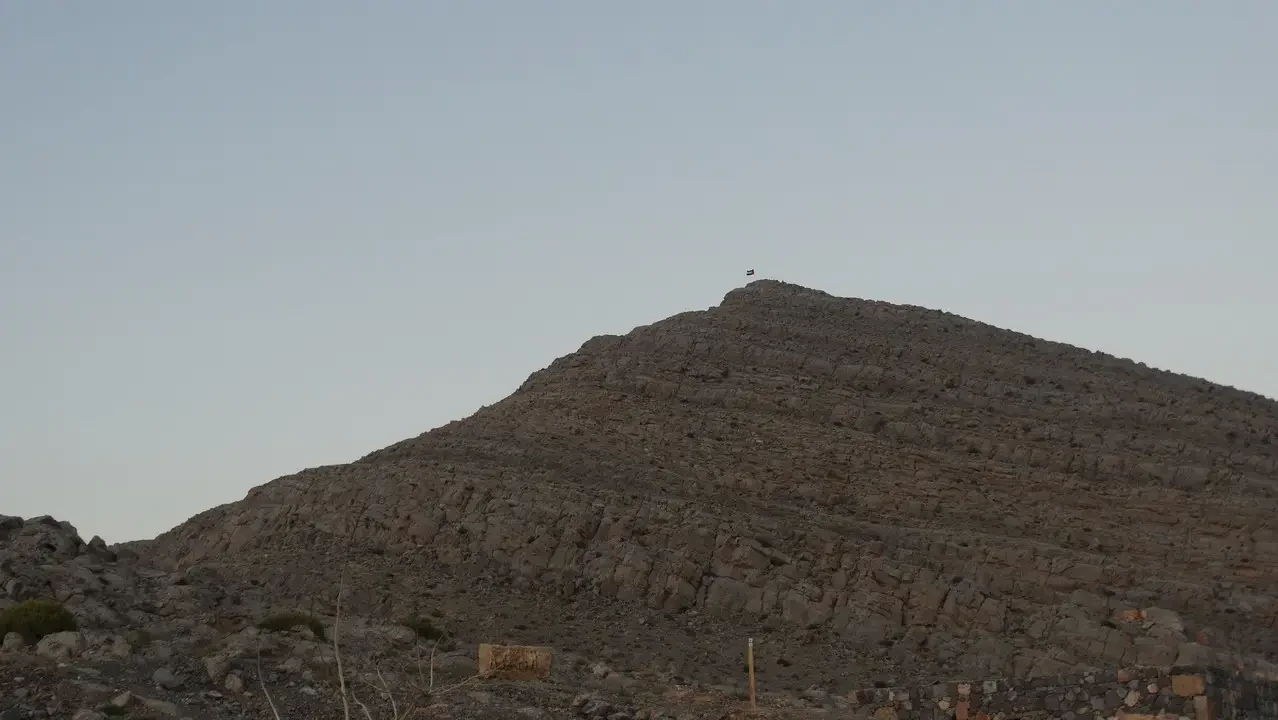 Una collina rocciosa si staglia nel paesaggio arido dell'Arabia.