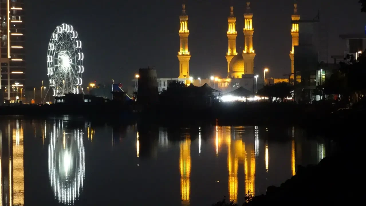 Sviluppo notturno dei minareti e di una ruota panoramica riflessi sull'acqua in Oman o negli Emirati Arabi Uniti.