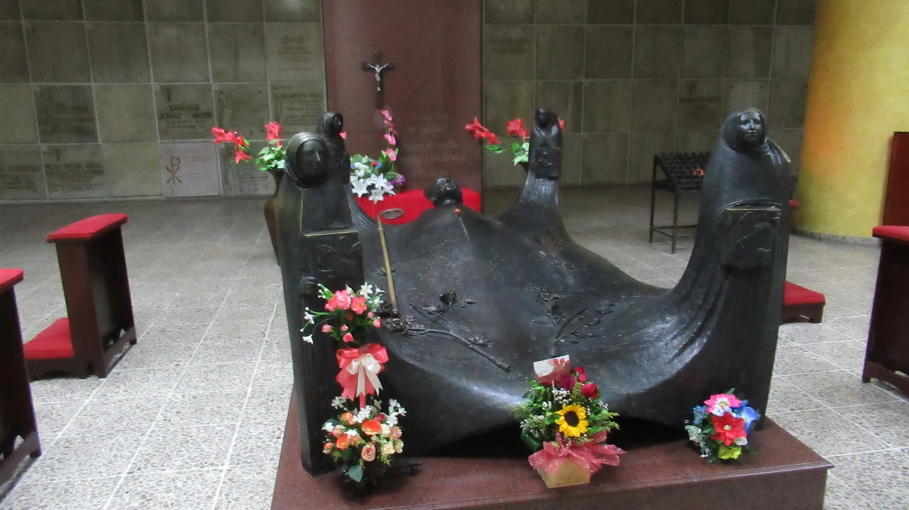Una scultura in bronzo raffigura una figura di Cristo sdraiata su un tronco, decorata con fiori.