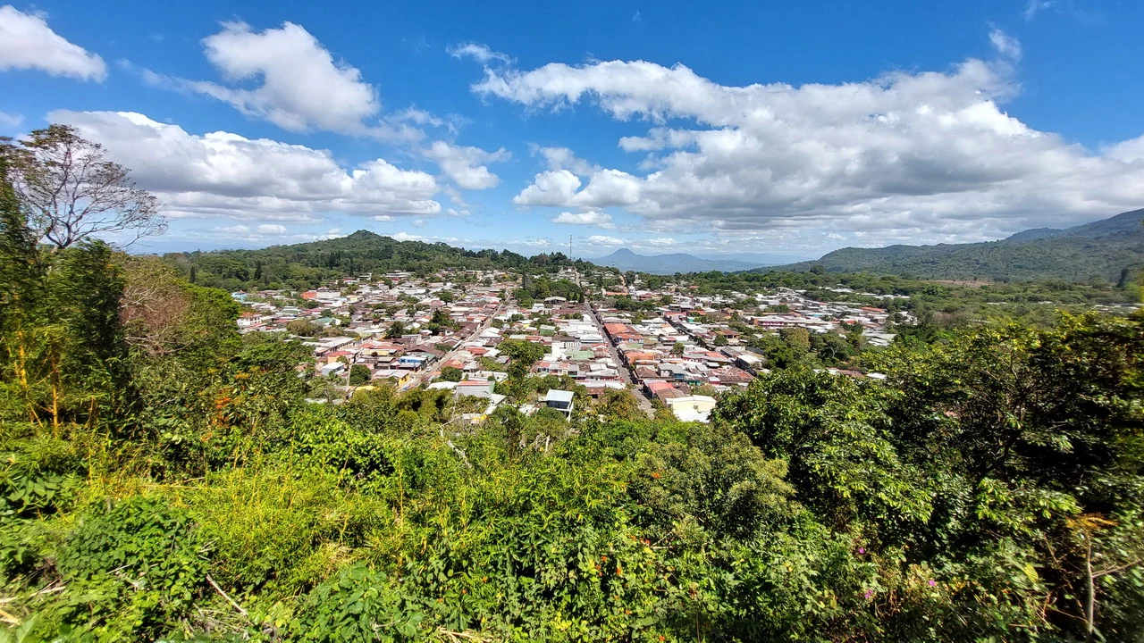 Vista panoramica di una città incastonata tra colline verdi sotto un cielo blu.
