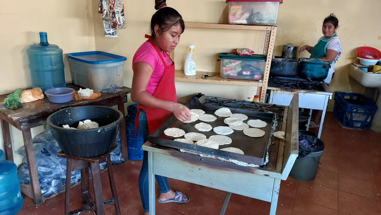 Donne stanno preparando tortillas su una piastra in un contesto rurale.