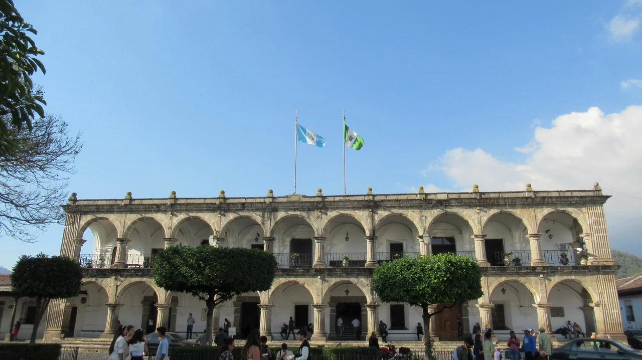 Vista frontale del municipio di Antigua Guatemala con edifici colonnati e bandiere sventolanti.