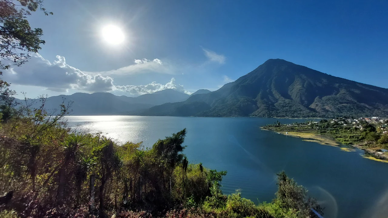 Paesaggio montano con un lago e montagne boscose sotto il sole brillante.