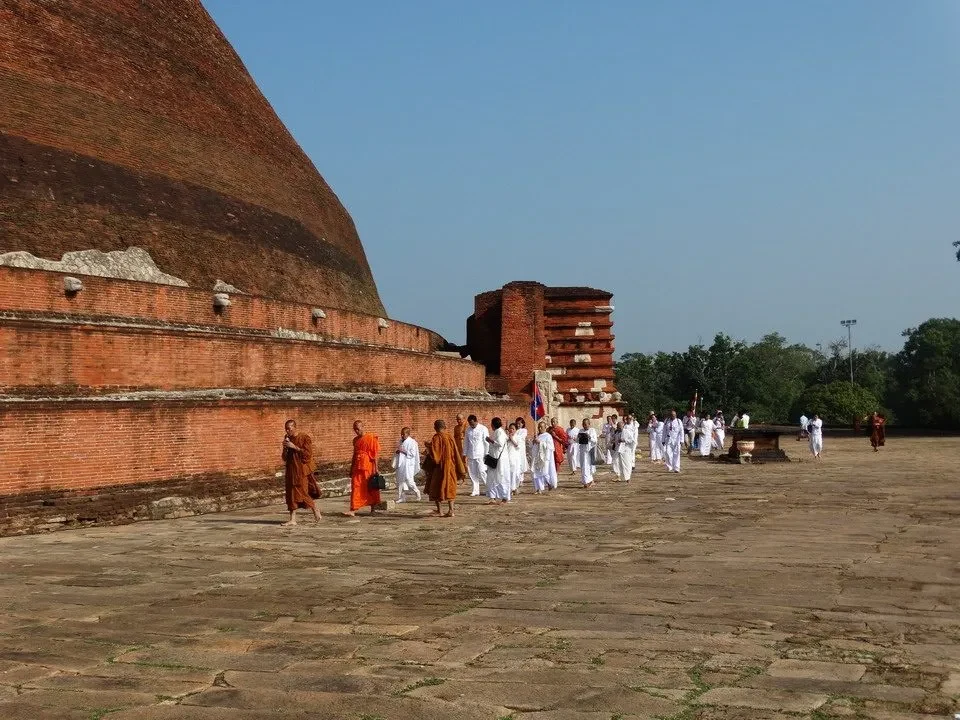 Rovine antiche di mattoni rossi con persone che passeggiano davanti a un antico sito religioso.