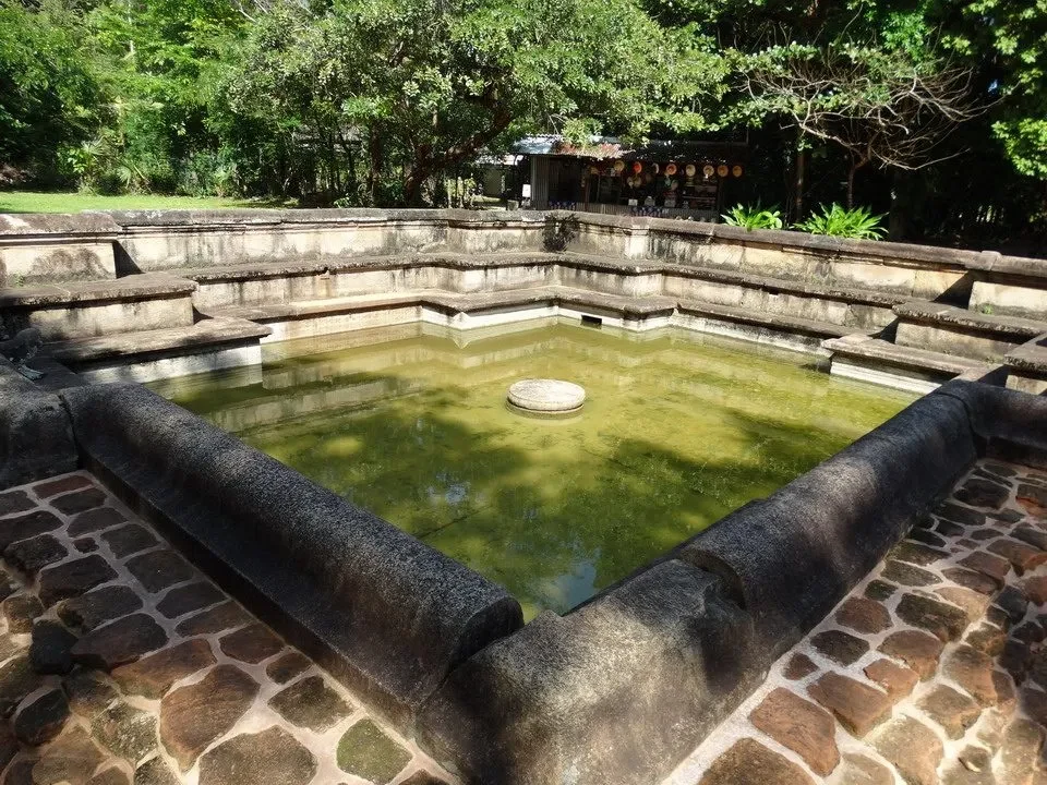 Una piscina antica circondata da mura in pietra e vegetazione.