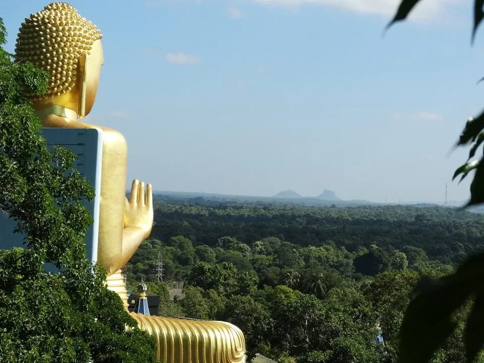Una grande statua dorata del Buddha sovrasta un vasto paesaggio verde.
