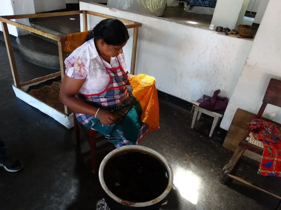 Una donna lavora in un laboratorio artigianale con materiali scuri.