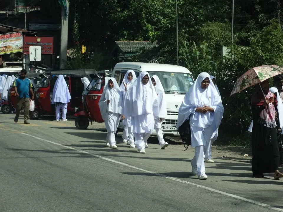 Un gruppo di persone cammina lungo una strada in Sri Lanka con ombrelli.