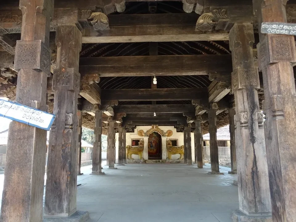 Interno di un antico tempio in legno con colonne e soffitto intagliato.