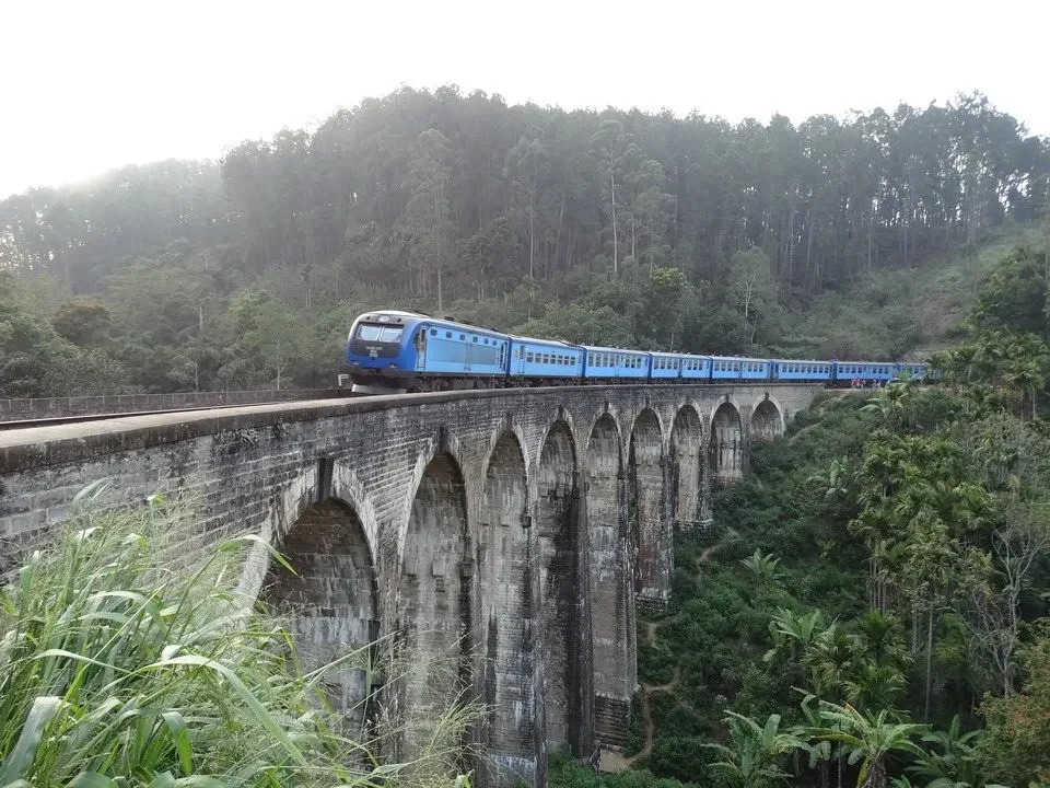 Treno blu attraversa un ponte in pietra attraverso una valle boscosa in Sri Lanka.