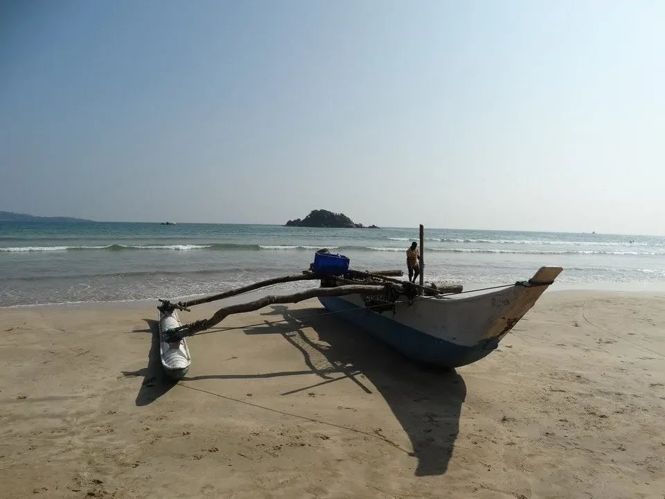 Una spiaggia di sabbia con una piccola barca ormeggiata e un uomo in piedi all'orizzonte.