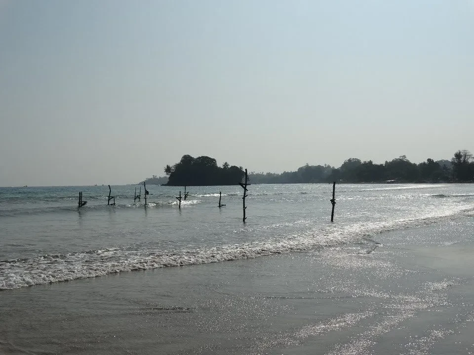 Una spiaggia tranquilla con onde bagnate e pali nell'acqua sotto un cielo luminoso.