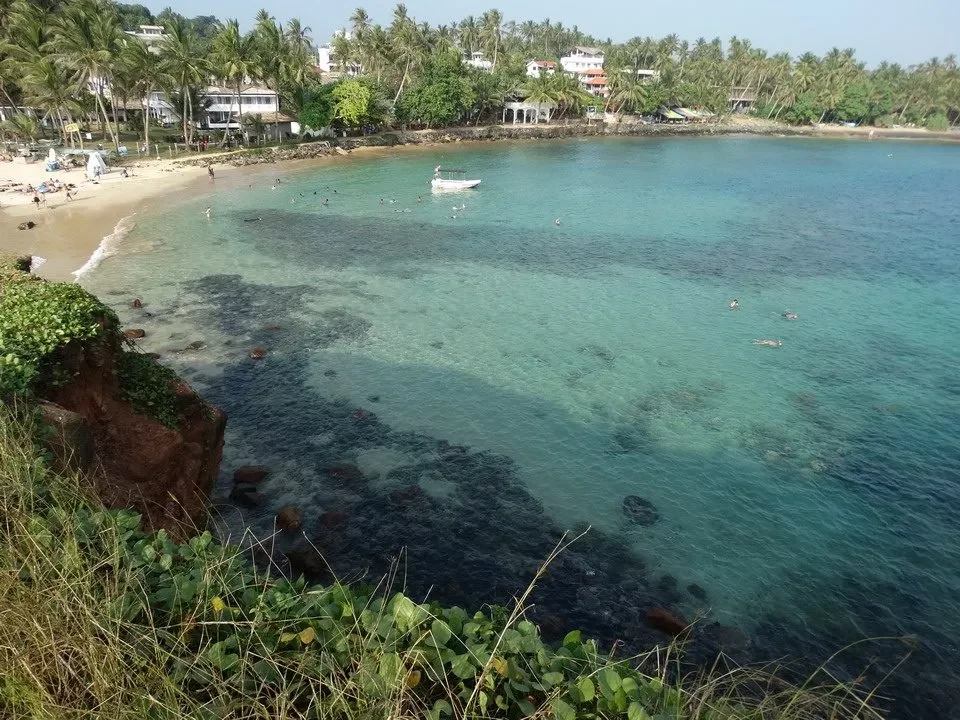 Una vista panoramica della spiaggia di Mirissa in Sri Lanka con acqua turchese e vegetazione lussureggiante.