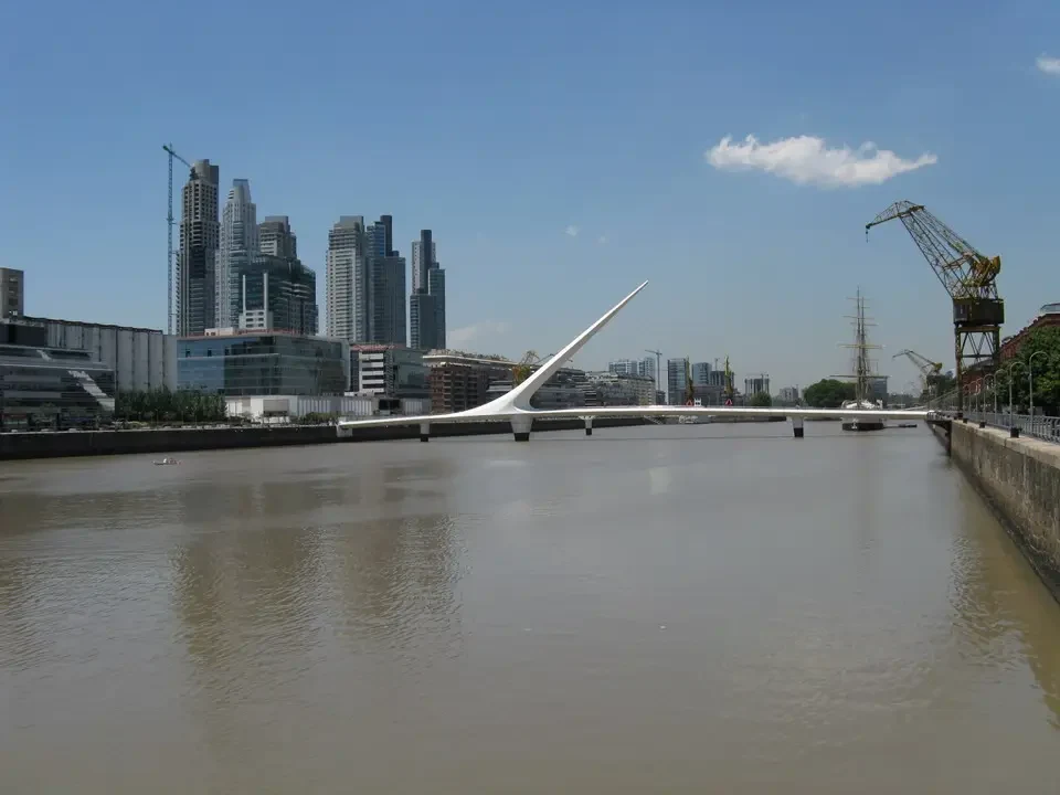 Un ponte moderno attraversa un fiume con edifici sullo sfondo.