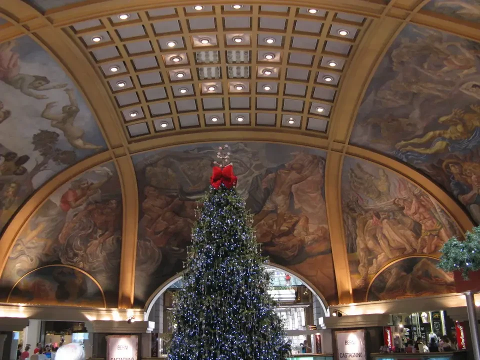 Albero di Natale illuminato in una sontuosa sala con soffitti decorati da affreschi classici.