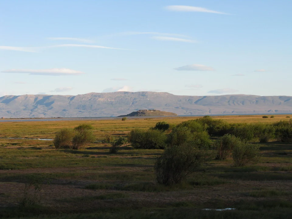 Paesaggio vasto della Patagonia con terreno pianeggiante e colline lontane sotto un cielo chiaro.