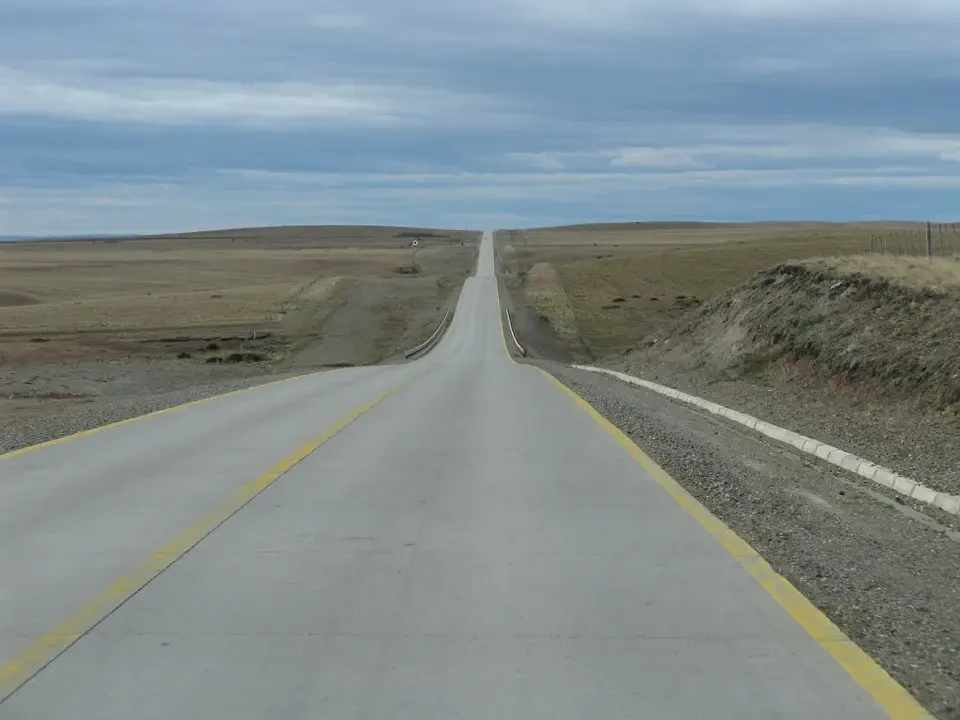 Una strada asfaltata si estende attraverso un paesaggio aperto della Patagonia sotto un cielo nuvoloso.