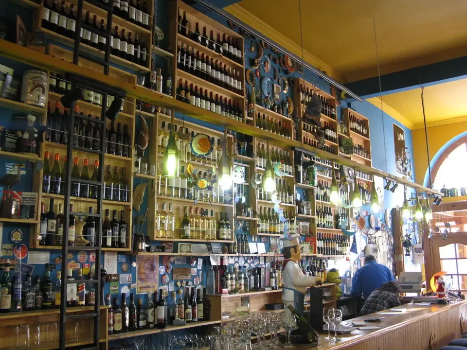Interno di un ristorante con scaffali pieni di bottiglie di vino e decorazioni artigianali.