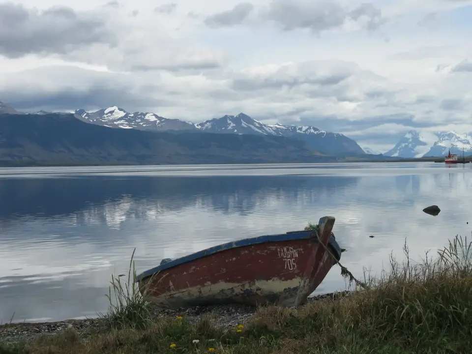 Un piccolo gommone è ormeggiato sulla riva di un lago patagonico con montagne innevate sullo sfondo.