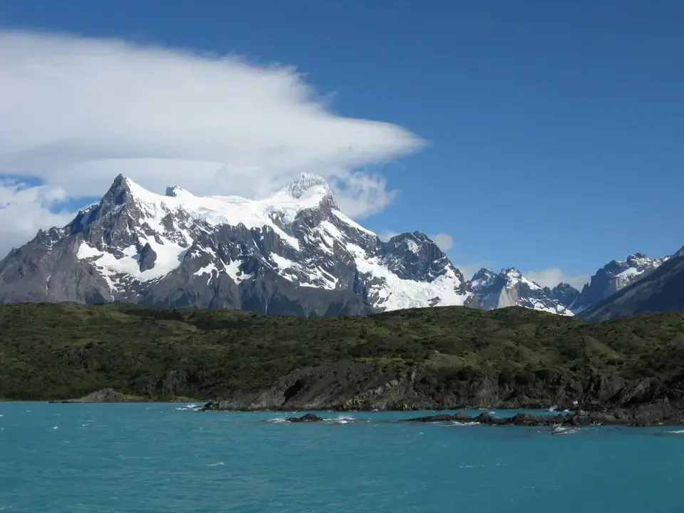 Le montagne innevate della Patagonia si stagliano sopra un corpo d'acqua turchese.