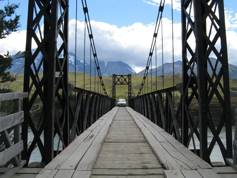 Ponte sospeso attraversa un fiume con montagne innevate in Patagonia.