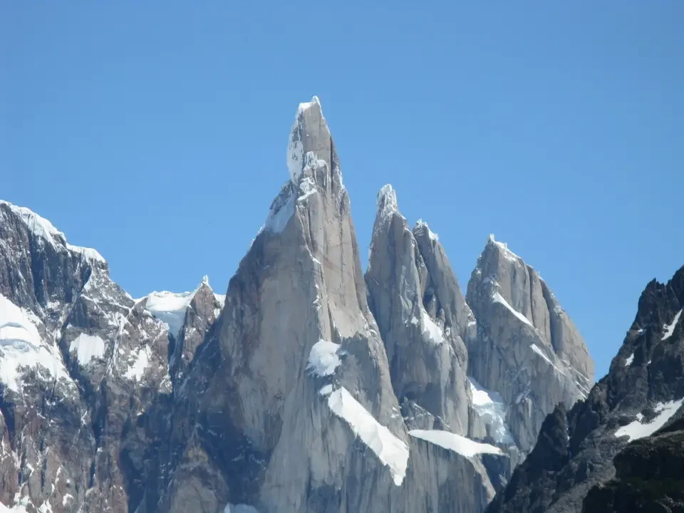 Una catena montuosa imponente con guglie rocciose innevate si staglia contro il cielo azzurro.