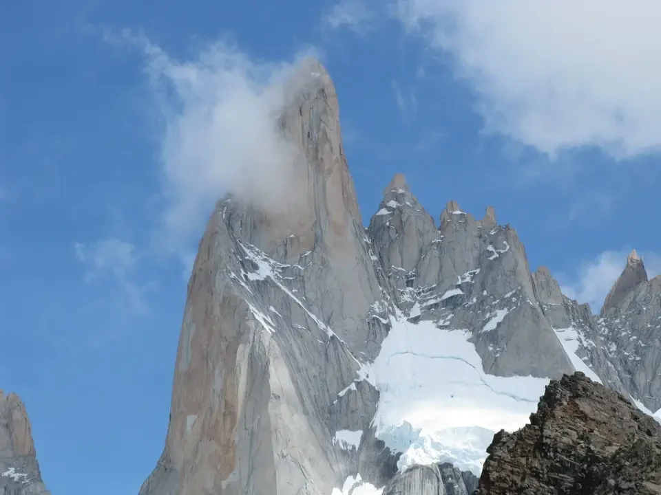 Una maestosa montagna innevata domina il paesaggio patagonico sotto un cielo azzurro con nuvole bianche.