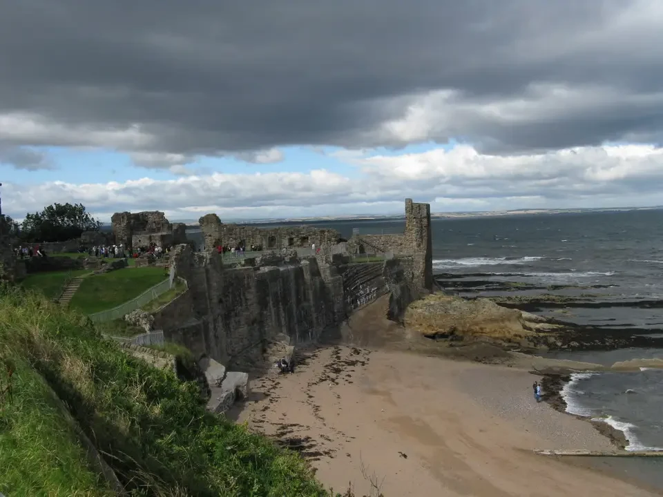 Le rovine del castello di St Andrews si estendono lungo la costa con un cielo nuvoloso.